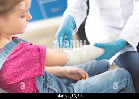 Doctor in white coat and medical gloves bandaging hand of little girl Stock Photo