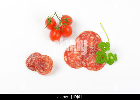 thin slices of salami with parsley and cherry tomatoes on white background Stock Photo