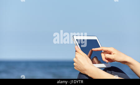 Close up picture of female finger touching screen of tablet computer on a beach, selective focus, space for text. Stock Photo