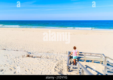 Young woman tourist standing on wooden platform and looking at sea on beautiful beach, Sylt island, Germany Stock Photo