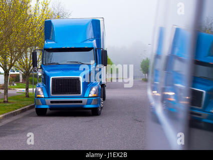 Professional blue semi truck with a spoiler on the roof and strict geometric headlights shape for stylish drivers parked on the road with spring trees Stock Photo