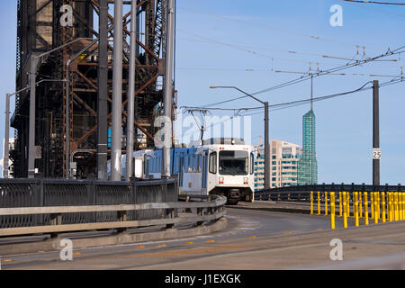 Modern white streetcar and power lines on the turn from the old drawbridge with rusty farm across the river Willamette in Portland Down Town Stock Photo