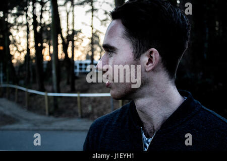 Young millennial man looks out to the future ahead of sunset through the woods Stock Photo