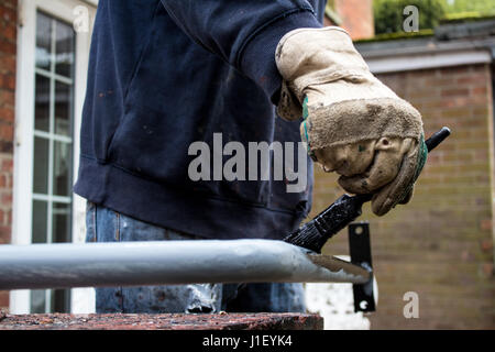 Painter decorator metalworker paints metal iron railing black with baggy jumper and workman’s gloves in back garden of residential job - BIY craftsman Stock Photo