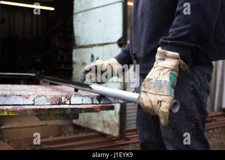 Painter decorator metalworker paints metal iron railing black with baggy jumper and workman’s gloves in back garden of residential job - BIY craftsman Stock Photo