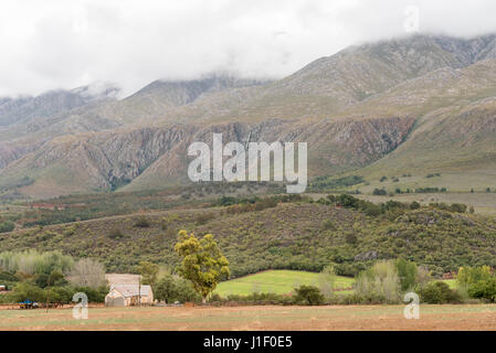 A farm landscape near Matjiesrivier with a waterfall in the back on the slopes of the cloud covered  Swartberg (black mountain) Stock Photo