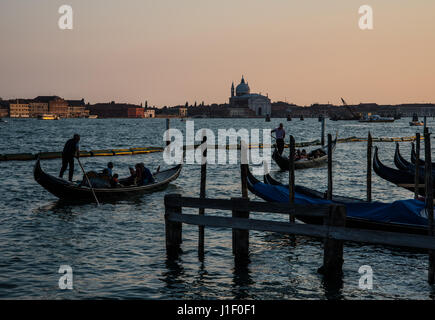 Gondoliers steering their gondolas into St Marks Basin to join line of moored gondolas with church of Santa Maria della Salute in background, Venice Stock Photo