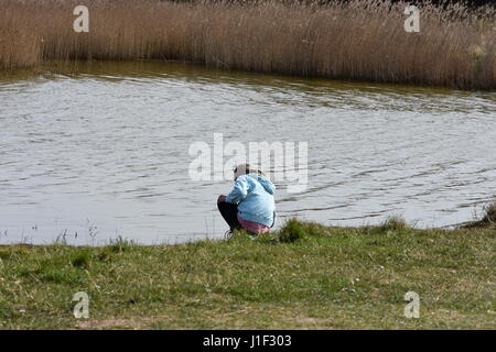 Girl crouching and looking at the lake at Snettisham, Norfolk, United Kingdom Stock Photo