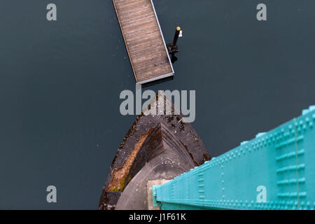 Modern Top view of the green support and concrete foundation of the bridge, the dark water and the wooden pier with a restrictive column. Avant-garde Stock Photo