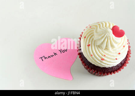 Cupcake with red heart and pink sticky note with handwriting words thank you with copy space on off white table Stock Photo
