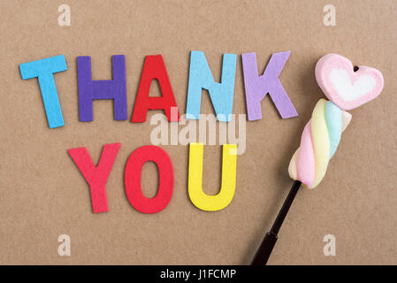 The colorful words thank you made with wooden letters with valentine heart candy on brown paper background Stock Photo