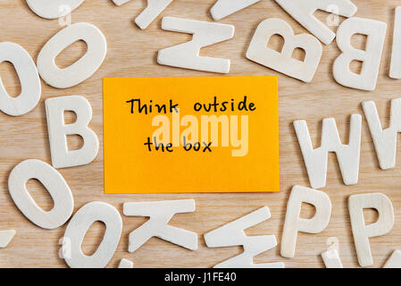 Handwriting letters words think outside the box on yellow sticky note with wood alphabet on wooden table, Quote Think different concept, Top view Stock Photo