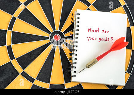 Red dart target arrow on open notebook with alphabet letters hand writing word what are you goal and question mask over dartboard background, Marketin Stock Photo