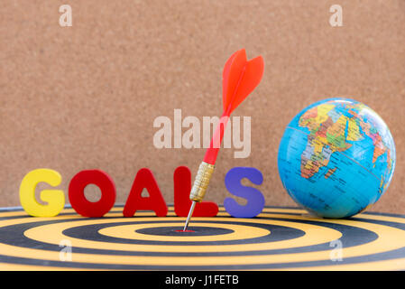 dart arrow hitting in target bullseye of center on dartboard with globe and word goals over wooden background with copy space, business marketing succ Stock Photo