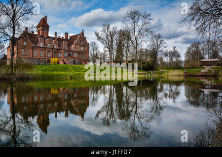 Jaunmoku castle near Tukums, Latvia reflecting in the lake. Beautiful blue sky and scenic clouds in the background on a sunny day. Postcard view. Stock Photo