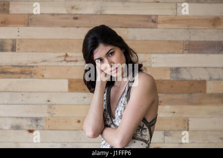 a brunette model wearing a dress against wood paneling with short hair and a fresh face with natural light shot on Canon in a studio. Stock Photo