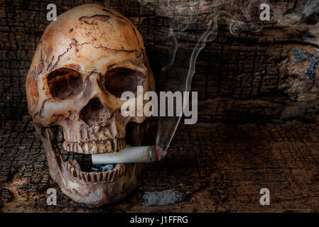 Human skull smoking cigarette with smoke on wooden background. Social issues smoking addiction concept, World no tobacco day please quit or stop smoke Stock Photo