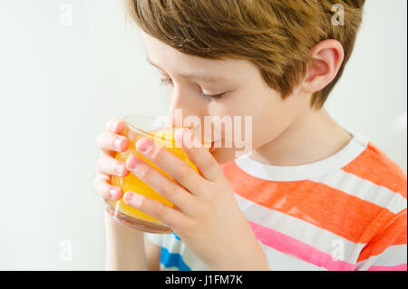 Young beautiful caucasian boy drinking orange juice from glass Stock Photo