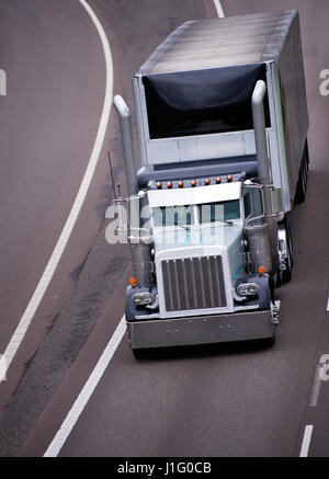 Thoroughbred classic stylish big rig semi truck with the custom personal tuning and high tailpipes on international highway with black tented trailer Stock Photo