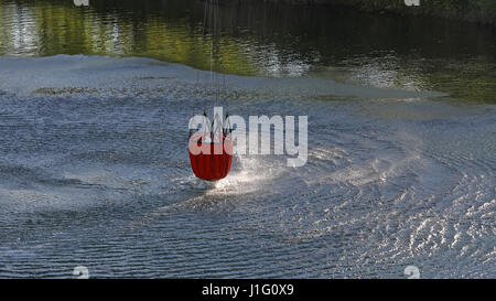 Detail of water bucket lifting out of the water under a helicopter with rotor wash on the surface of the lake Stock Photo