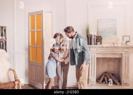 Happy family embracing and standing at home with fireplace behind Stock Photo