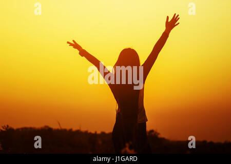 Happy woman raised hands up on the sky at sunset Stock Photo