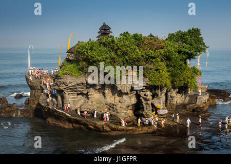 Balinese Hindus pilgrimage to Tanah Lot rock temple. Beautiful aerial view of the famous rock temple receiving many pilgrims in traditional clothes Stock Photo