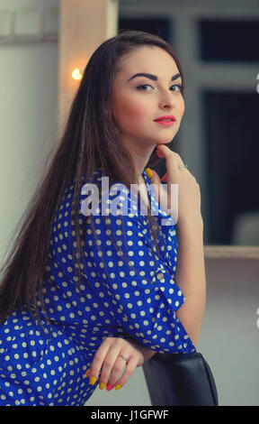 Young cheerful girl in blue dress in white polka dot posing in studio. Stock Photo