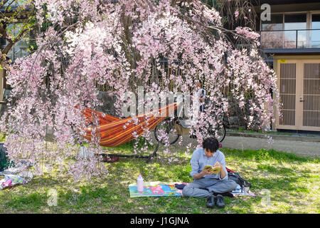 A man relaxes under a cherry blossom tree in Kyoto, Japan, during the 'sakura' season in 2017. Stock Photo