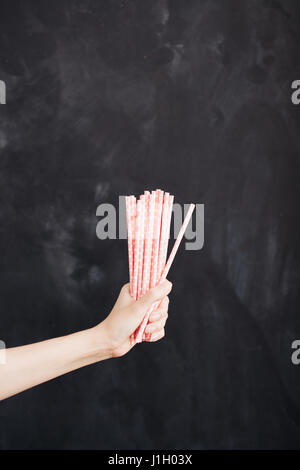 Woman hand hold cocktail straw on black background. Stock Photo