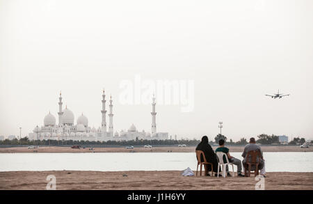 ABU DHABI, UNITED ARAB EMIRATES - April 27, 2012: A family sits beside the water over looking the Sheikh Zayed Grand Mosque in Abu Dhabi. Stock Photo