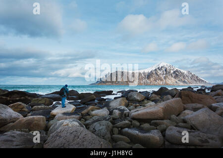 The photographer is shooting the high wave on a stony coast in the background of a snowy mountain in the Lofoten Islands Stock Photo