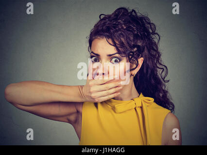 Closeup portrait of scared young woman covering with hand her mouth isolated on gray wall background Stock Photo