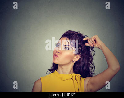 Portrait confused thinking young woman bewildered scratching her head seeks a solution looking up isolated on gray wall background. Human face express Stock Photo