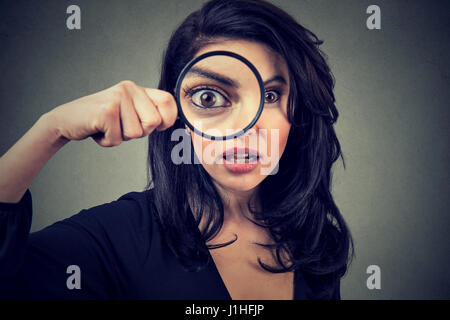 Surprised woman looking through magnifying glass isolated on gray wall background. Stock Photo