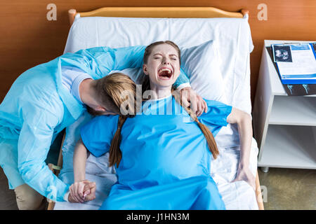 pregnant woman giving birth in hospital while man hugging her Stock Photo