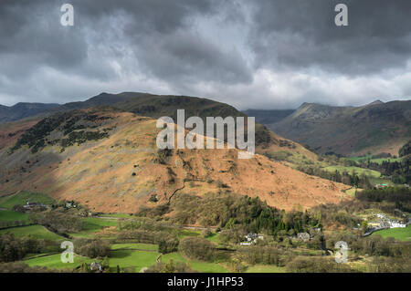 view over sunlit green fields towards Arniston Crag and Black Crag across Patterdale valley from the slopes of Patterdale Common, Lake District Stock Photo