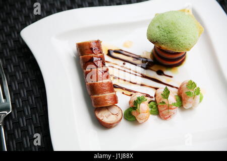 A restaurant dish of pork and prawns served with a stack of vegetables and foam Stock Photo