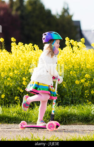 Child riding scooter on way back to school. Little girl playing outdoors learning to balance on kick board. Kids ride scooters in suburbs street. Pres Stock Photo