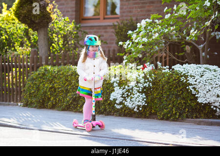 Child riding scooter on way back to school. Little girl playing outdoors learning to balance on kick board. Kids ride scooters in suburbs street. Pres Stock Photo