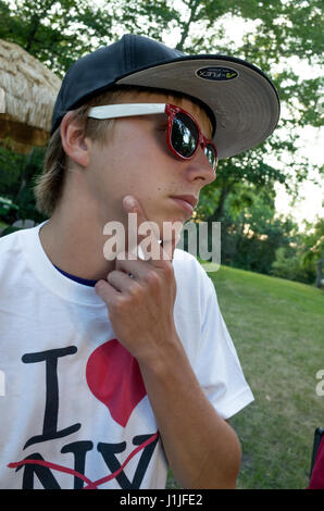 Teen boy enjoying outdoor summer vacation wearing cool sunglasses in a thoughtful pose. Teenage male age 15. Clitherall Minnesota MN USA Stock Photo