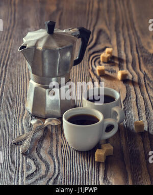 Two cups of coffee with pieces of cane sugar and Italian  coffee maker on wooden table.  Toned image.