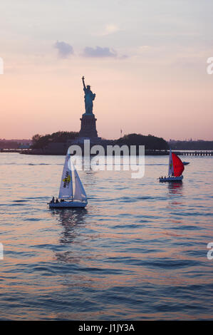 The statue of liberty in sunset, as retirement yachts are sailing into New York Harbour.  Sailing clubs are the best way to enjoy retirement. Stock Photo