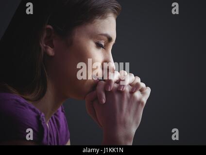 Digital composite of Woman praying against dark grey background Stock Photo