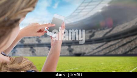 Digital composite of Woman touching blank screen of mobile phone at stadium Stock Photo