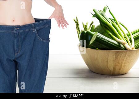 Digital composite of Midsection woman in loose jeans by vegetables Stock Photo