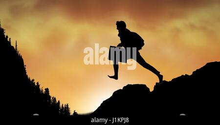 Digital composite of Silhouette businessman jumping on mountain against sky Stock Photo