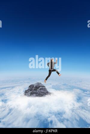 Business man jumping off mountain peak in the clouds Stock Photo