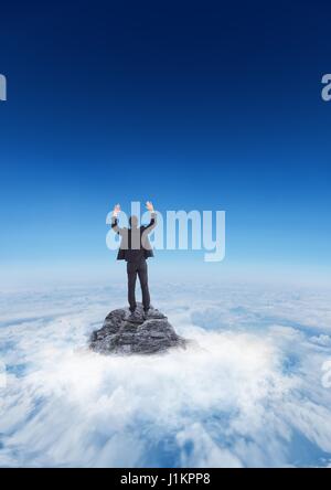 Digital composite of Business man cheering on mountain peak in the clouds Stock Photo
