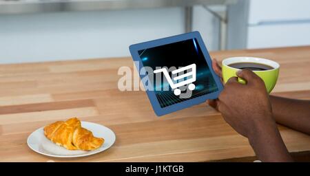 Digital composite of Cropped image of person holding digital tablet with shopping cart icon on screen while having coffee Stock Photo